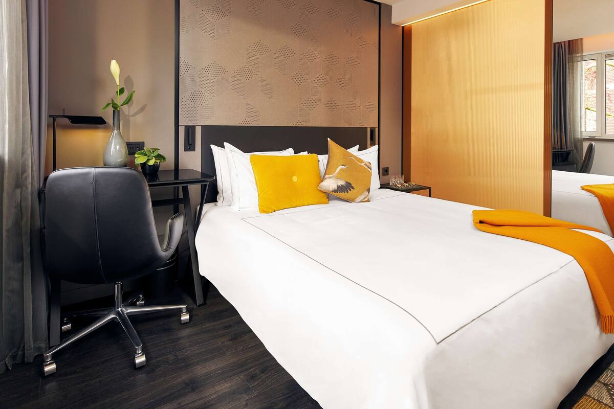 Una habitación de hotel con cama, escritorio, silla y ventana.