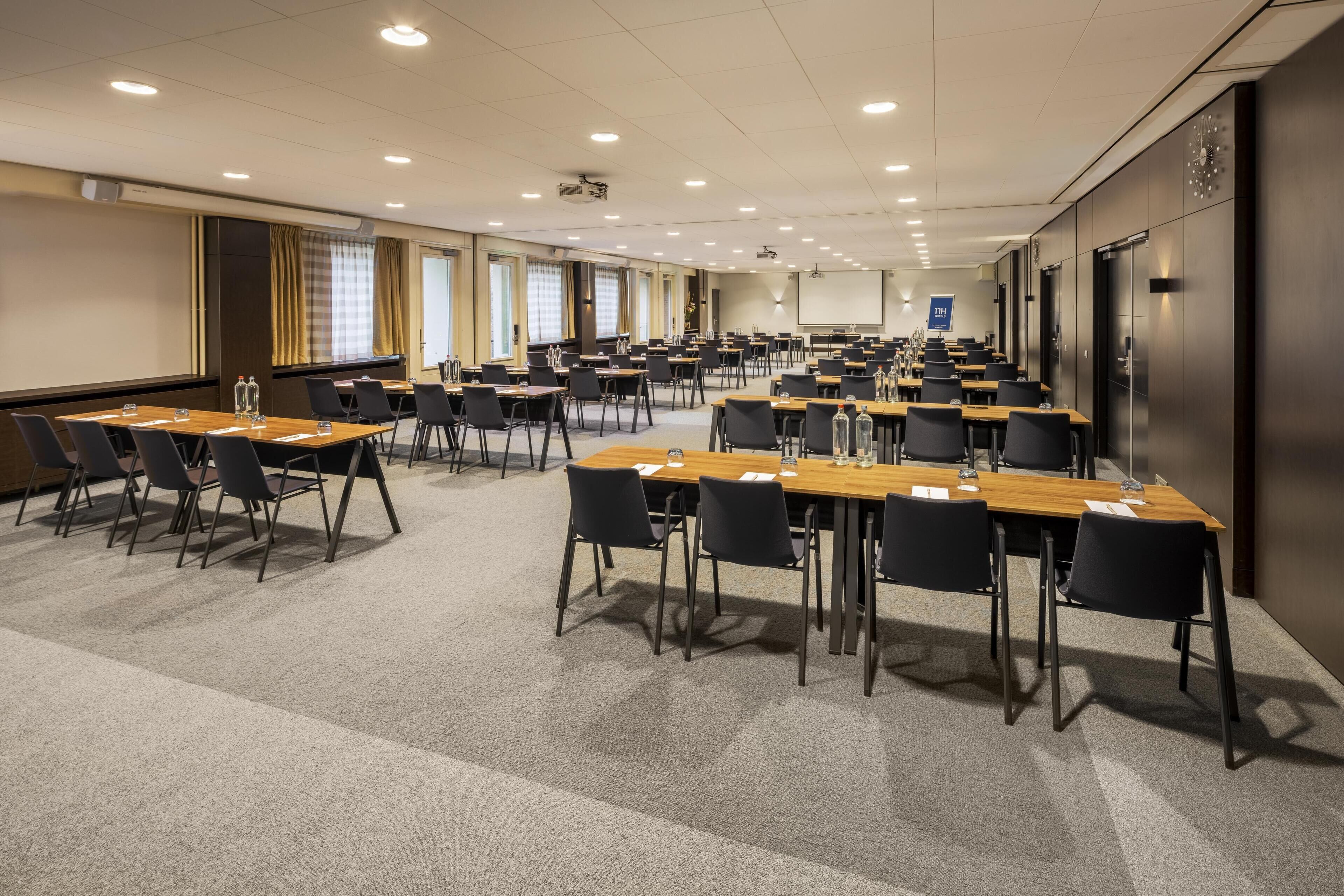 Een ruime congreszaal met meerdere tafels en stoelen, voorzien van projectoren en schermen.