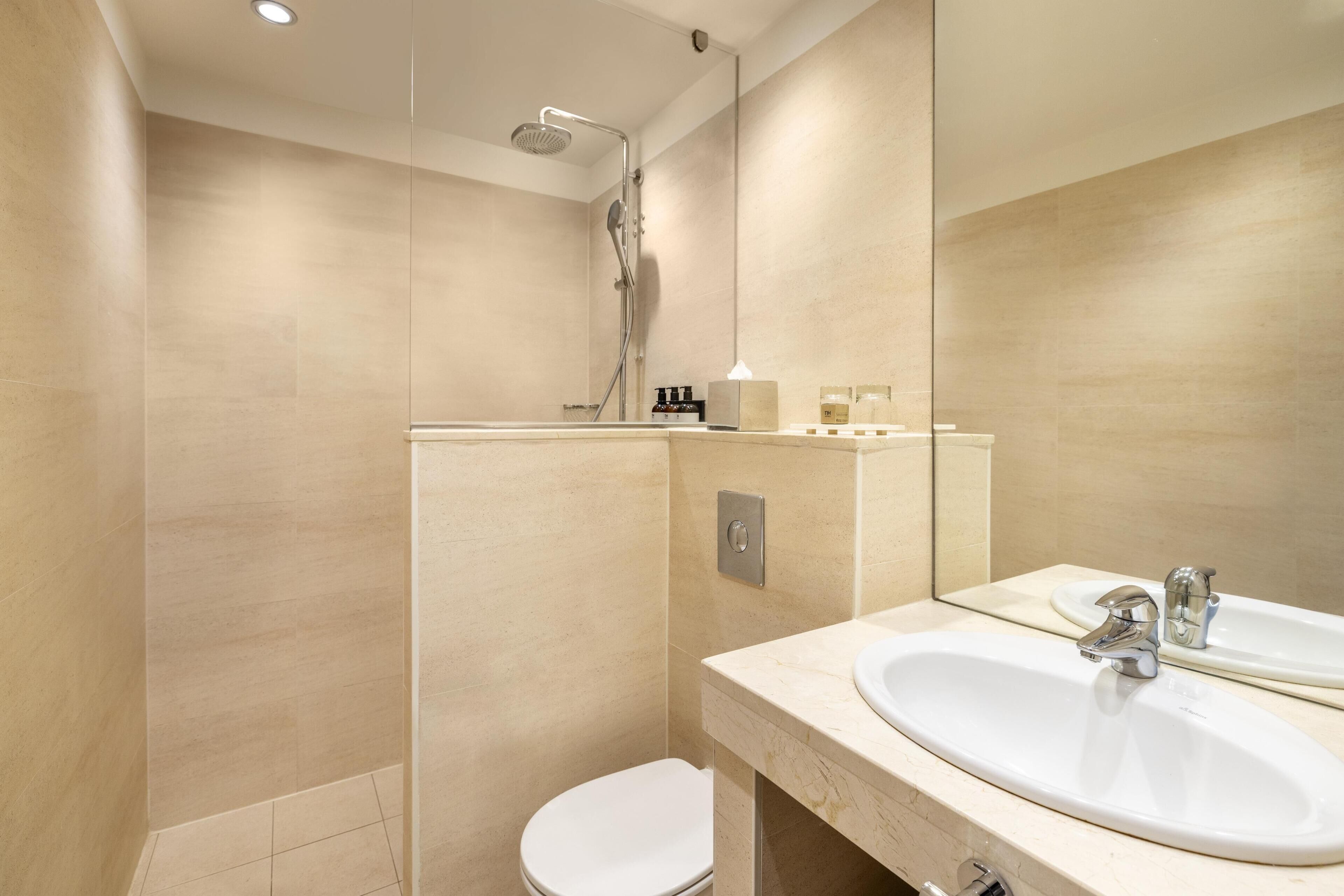 A modern bathroom with a large mirror, two sinks, a shower, and a toilet.