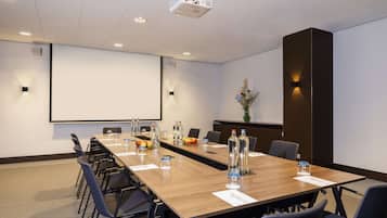 Uma sala de conferências com uma mesa comprida, cadeiras, uma tela de projetor e um arranjo floral.