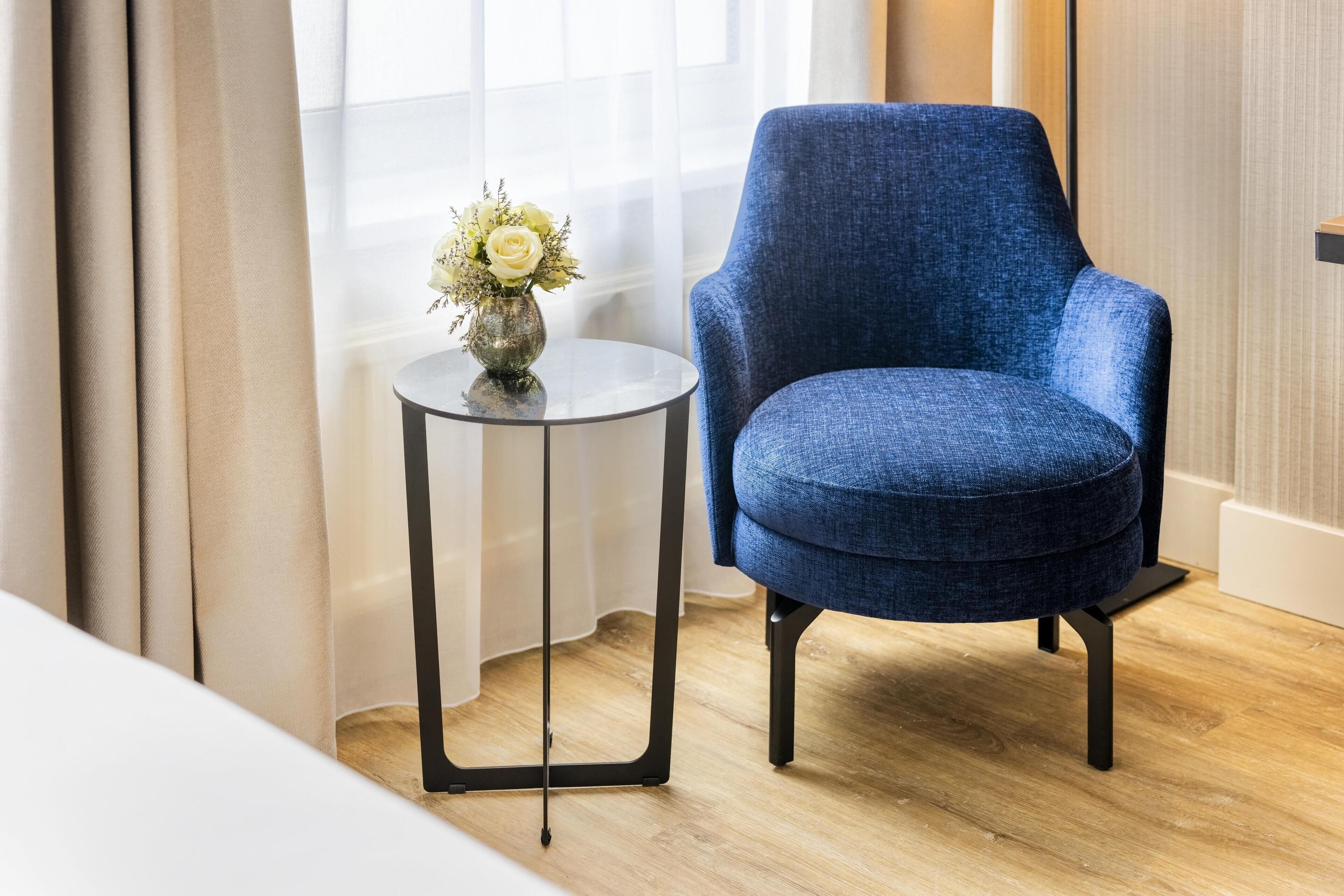 A blue armchair next to a small round table with a vase of flowers.