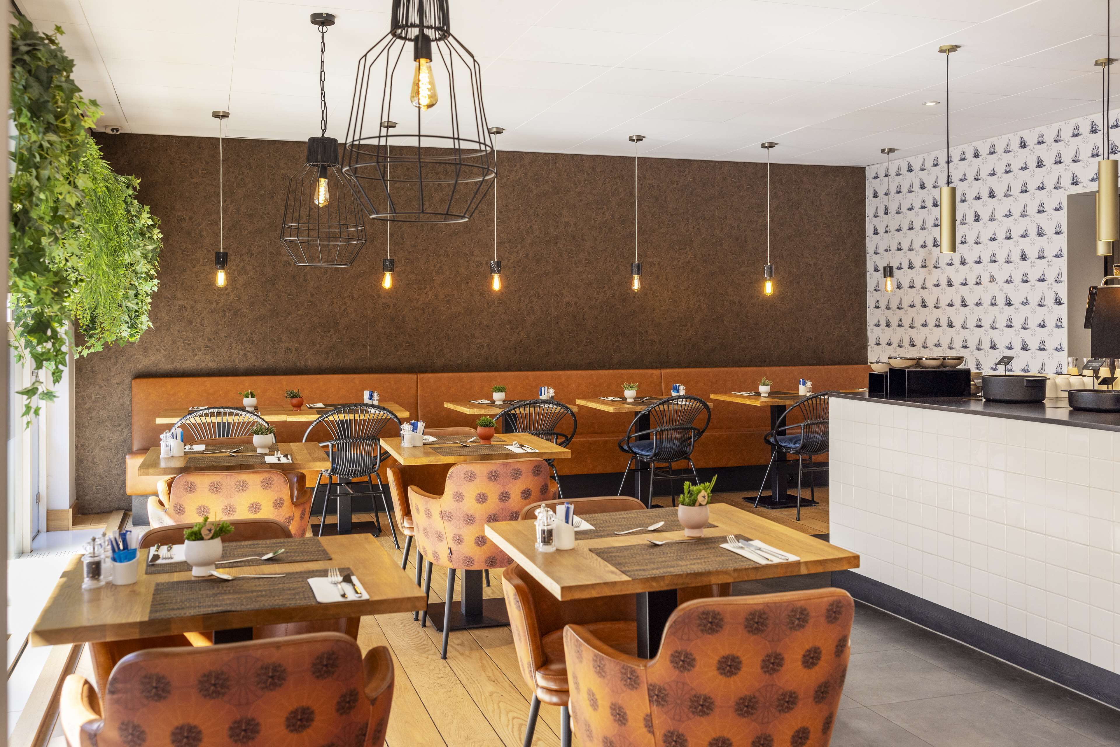 Un restaurante con mesas de madera y sillas estampadas, lámparas colgantes y un muro decorado.