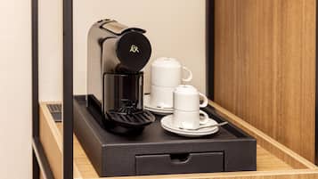 A coffee machine on a tray with two white cups and a saucer.