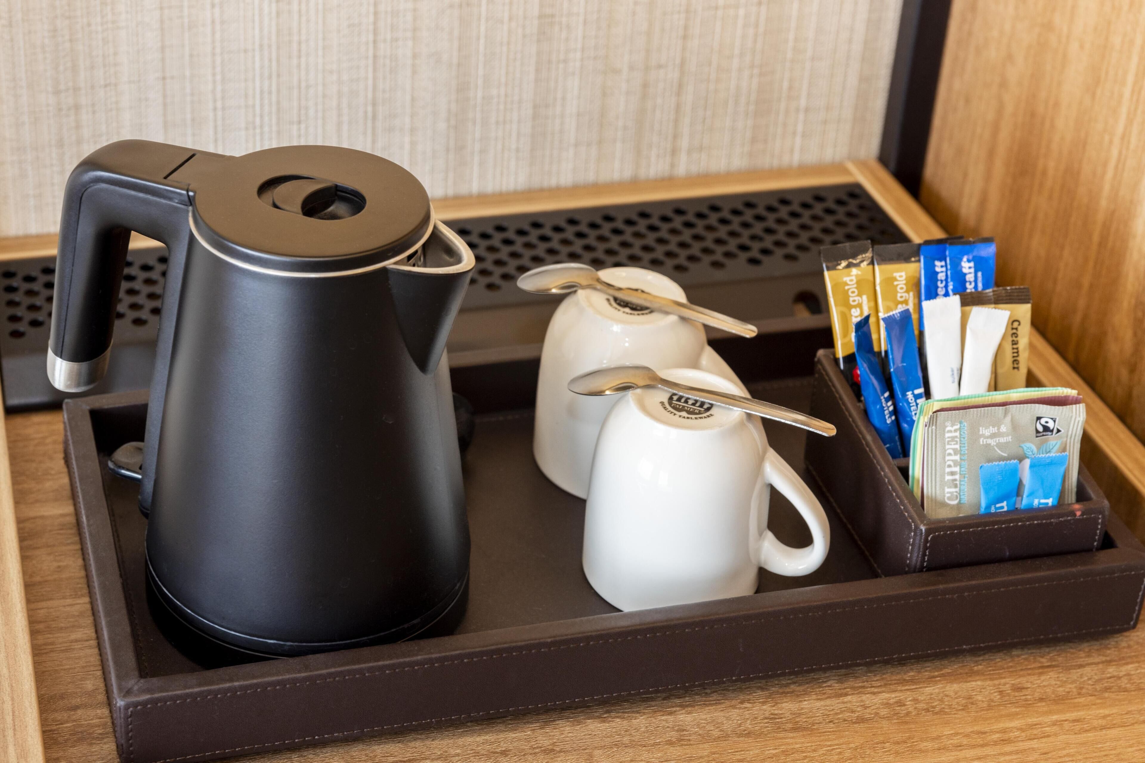 A tray with a black electric kettle, two white mugs, and a set of toiletries including a toothbrush, toothpaste, and a razor.