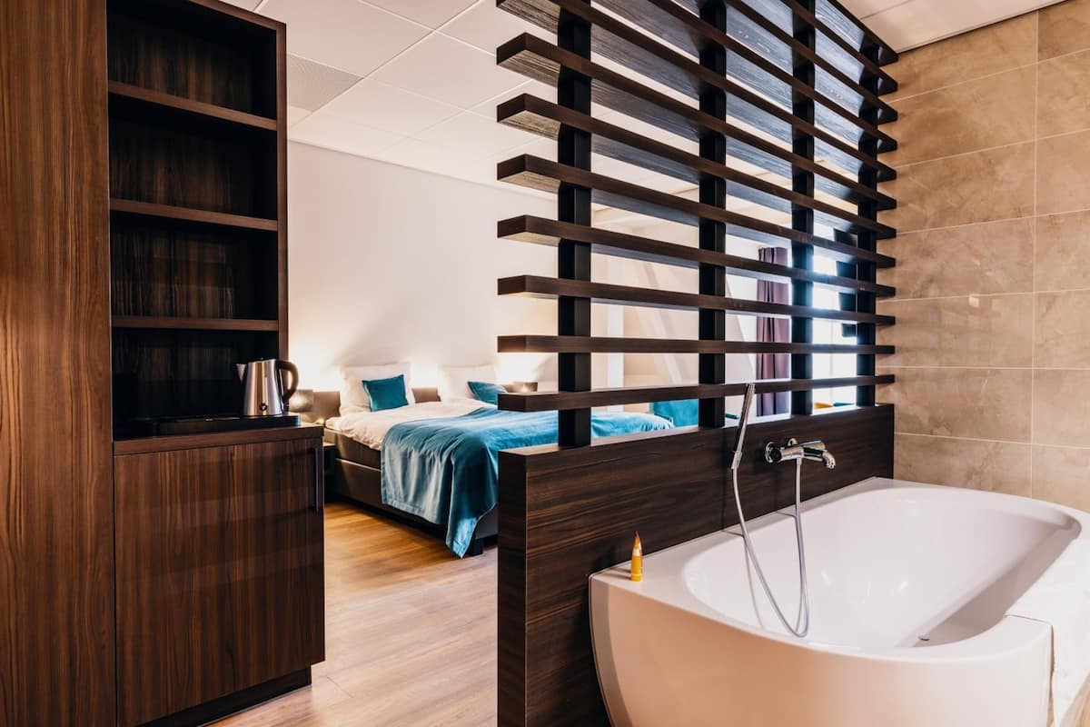 A modern bedroom with a large bed, a wooden wardrobe, and a bathroom with a bathtub.