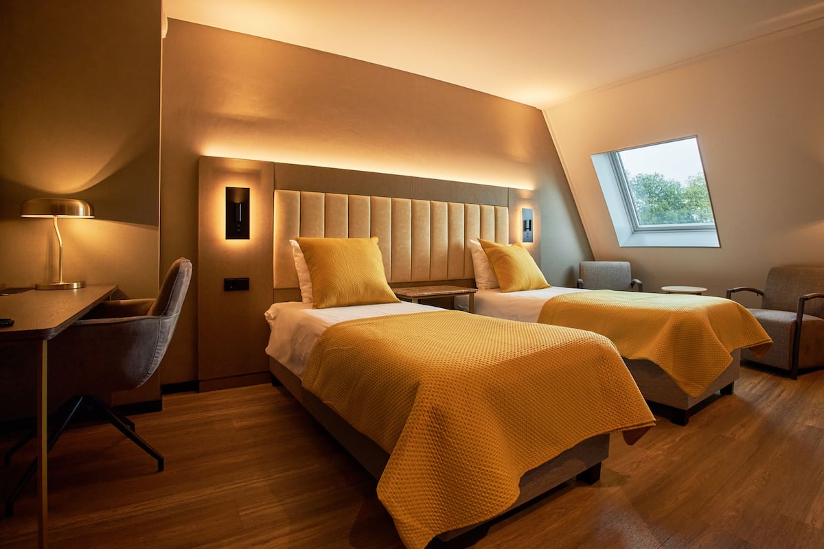 A modern hotel room with two beds, a desk, and a chair.