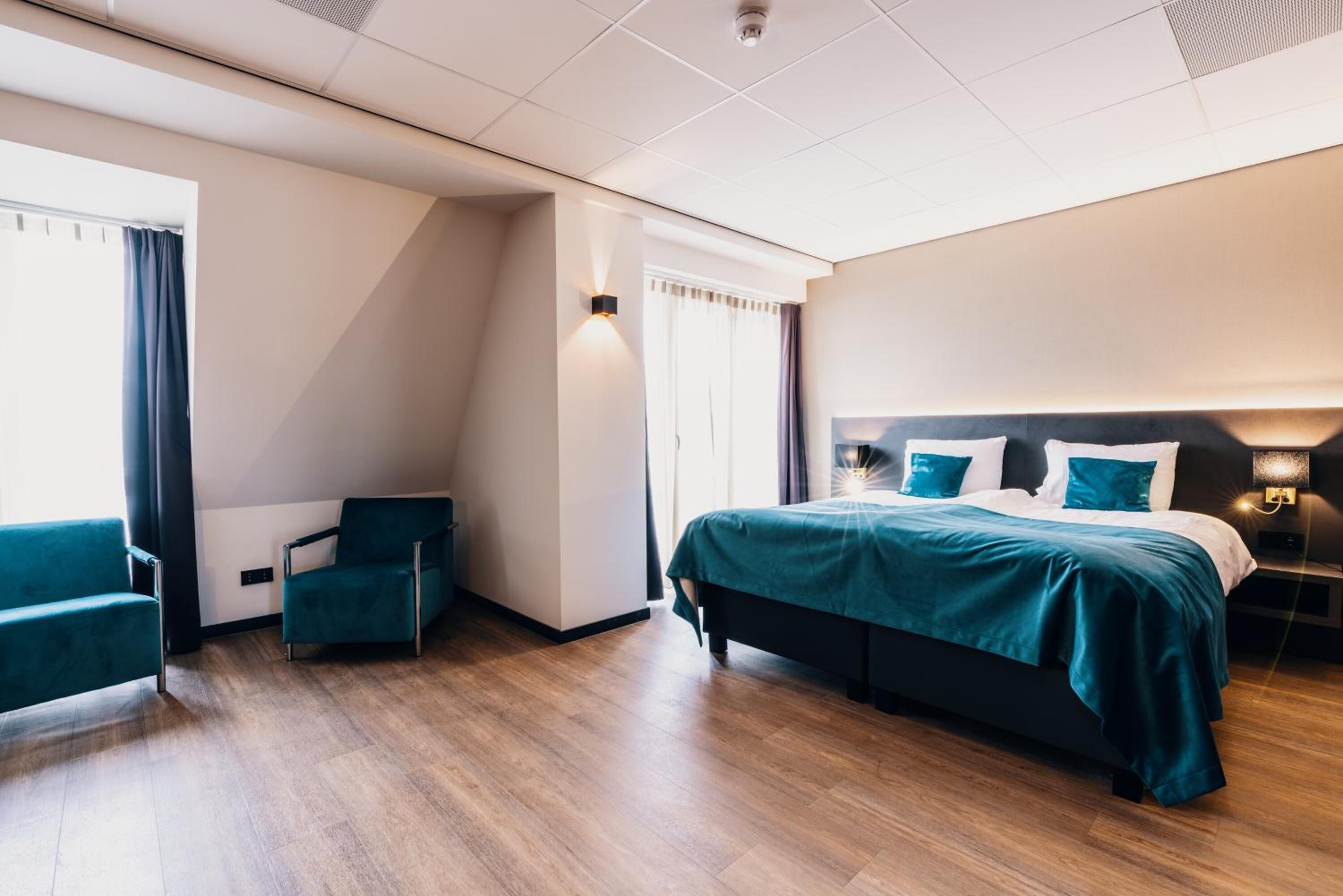 Een moderne hotelkamer met een groot bed, een zithoek met een stoel en uitzicht op het omliggende landschap.
