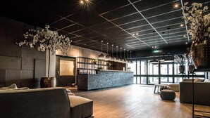 A modern lobby with a wooden floor, a reception desk, and a seating area with sofas and a large vase of flowers.