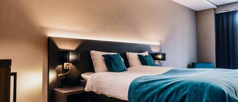 Una habitación de hotel moderna con cama, mesitas de noche y cabecera con iluminación integrada.