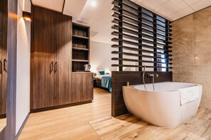 A modern bathroom with a freestanding bathtub, wooden cabinetry, and a built-in shelf unit. - Hotel Hoogeveen (Hoogeveen)