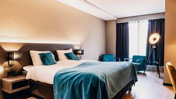 A modern hotel room with a large bed, a desk, a chair, and a desk lamp.