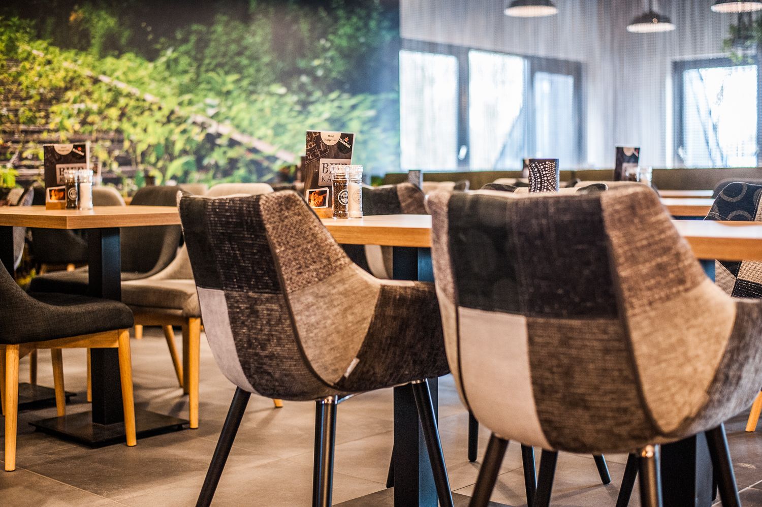 L’intérieur d’un restaurant moderne est agrémenté de tables et de chaises en bois, d’une grande fenêtre offrant une vue sur la verdure et d’un présentoir à menus.