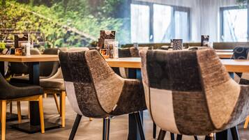 L’intérieur d’un restaurant moderne est agrémenté de tables et de chaises en bois, d’une grande fenêtre offrant une vue sur la verdure et d’un présentoir à menus.