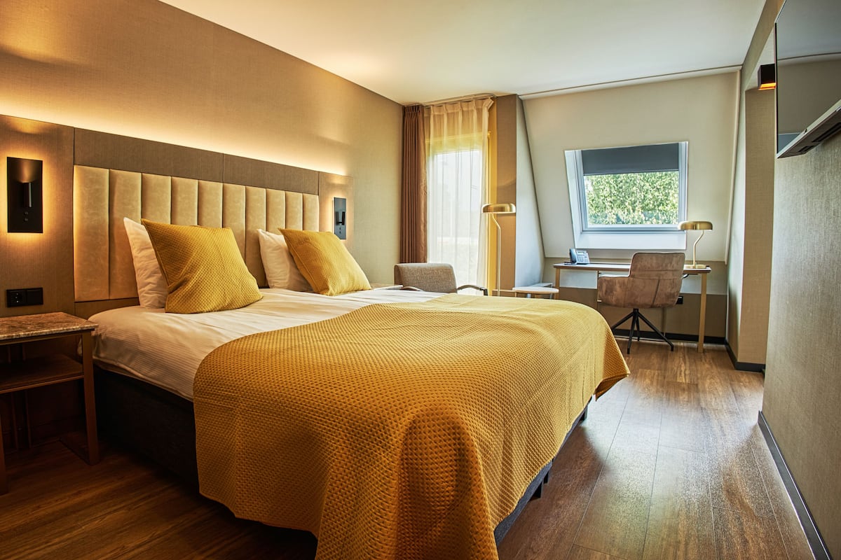 A hotel room with a large bed, a desk, and a chair.