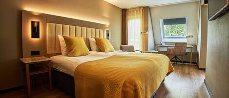 A hotel room with a large bed, a desk, and a chair.