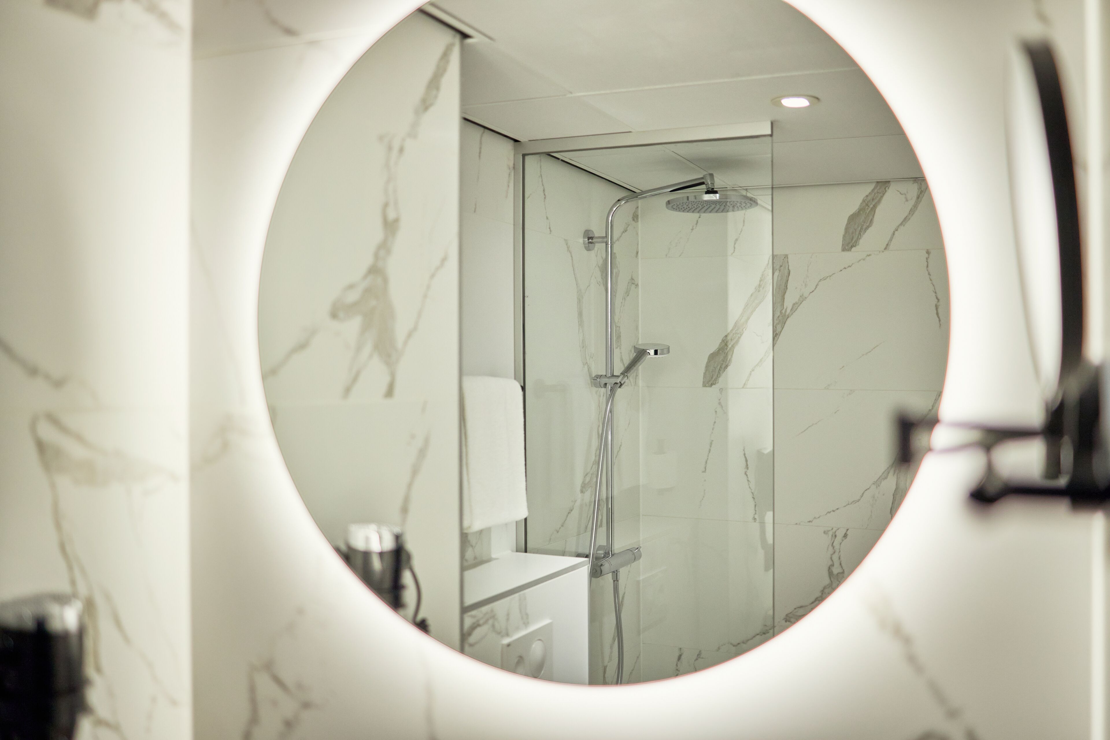 Ein modernes Badezimmer mit einem runden Spiegel, Marmorwänden, einer Dusche und einem WC.