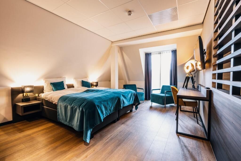 A modern hotel room with a large bed, a desk, and a chair. There is a window with curtains and a view of the outside.