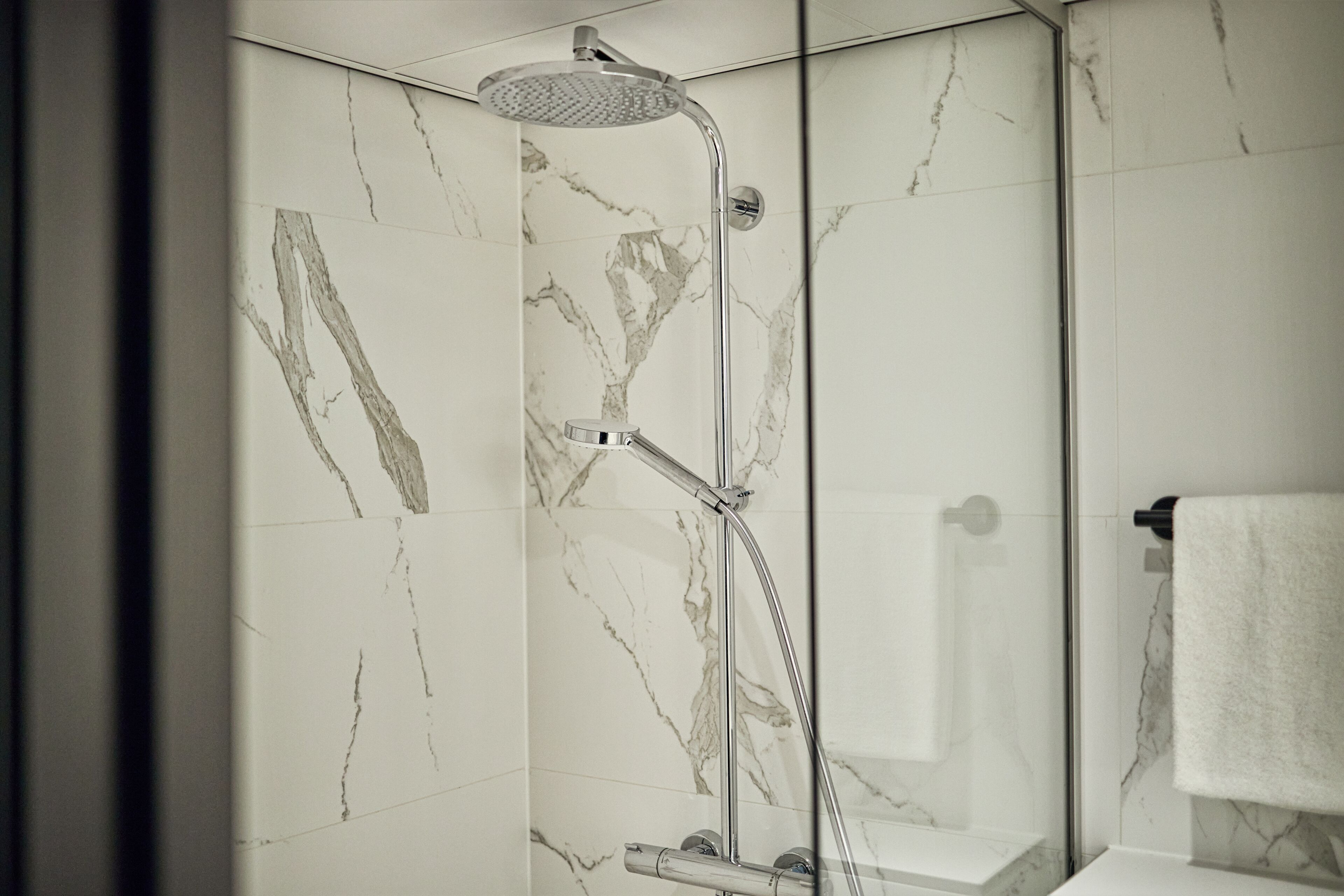 Une salle de bain moderne avec une douche à parois de verre, des murs en marbre et une serviette blanche posée sur un porte-serviettes.