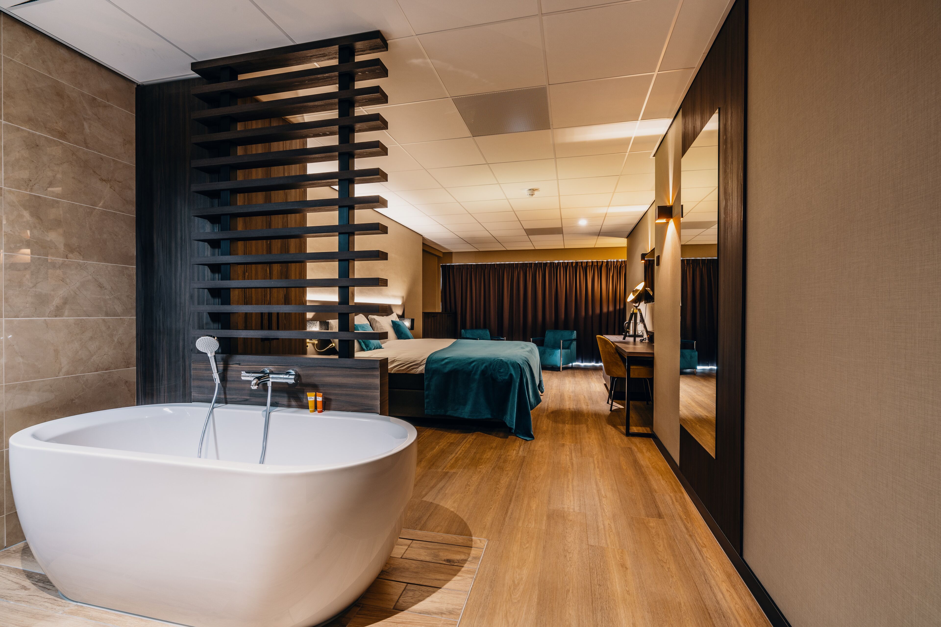Un baño moderno con una bañera independiente grande, un revestimiento de pared de listones de madera y una zona de tocador con espejo.