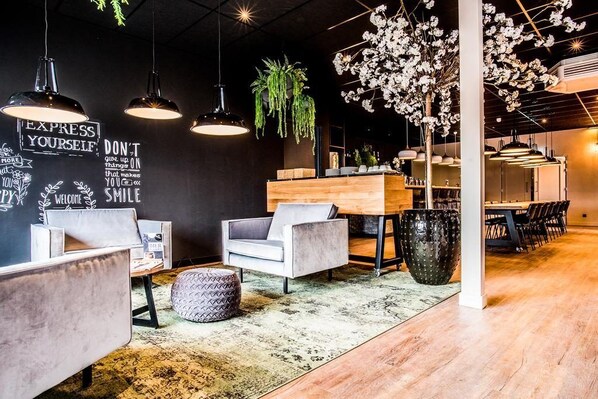 A modern interior with a reception desk, seating area, and decorative plants. - Hotel Hoogeveen (Hoogeveen)