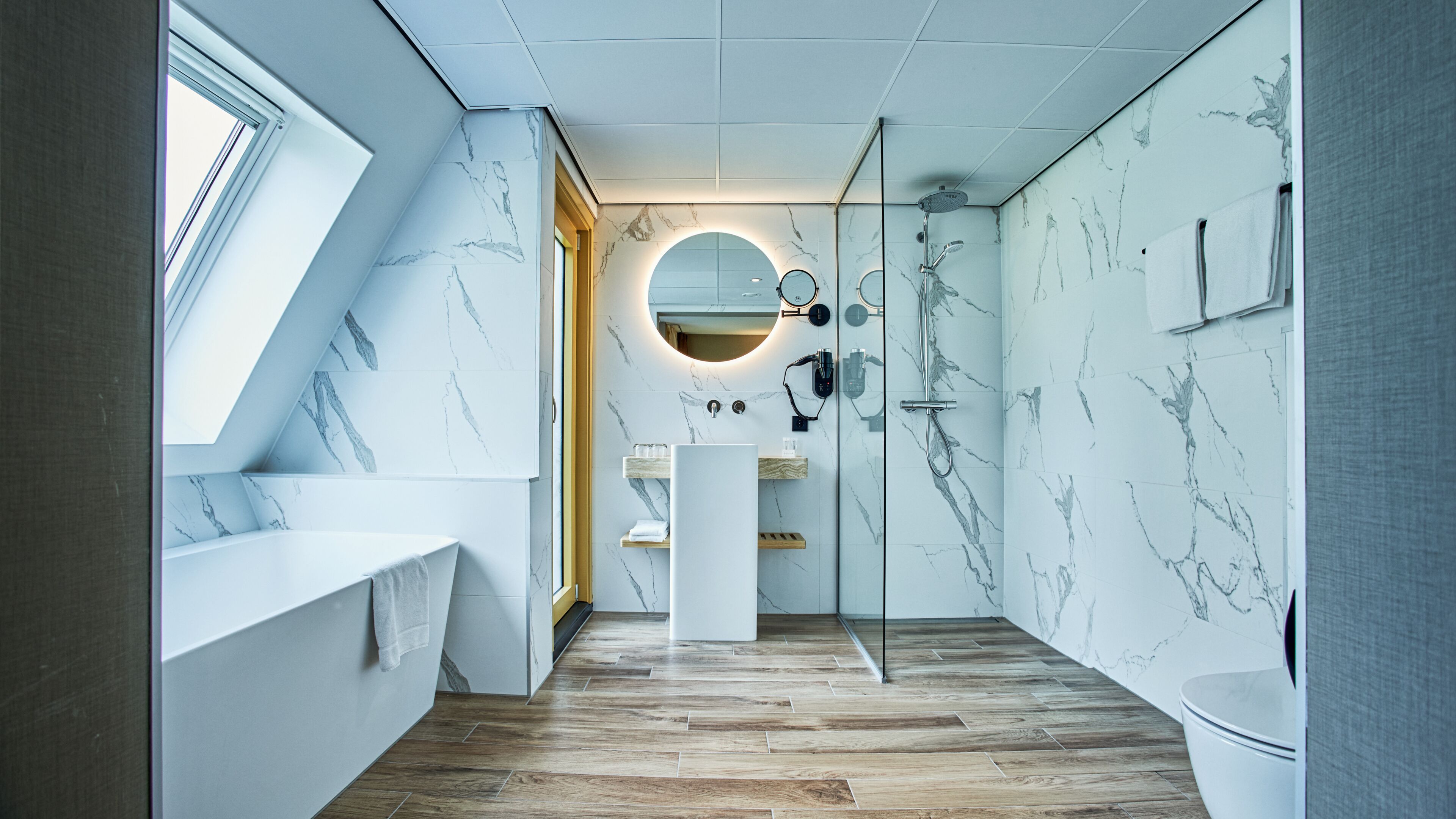 Un bany modern amb un fanal, parets de marbre, un lavabo central i una zona de dutxa.