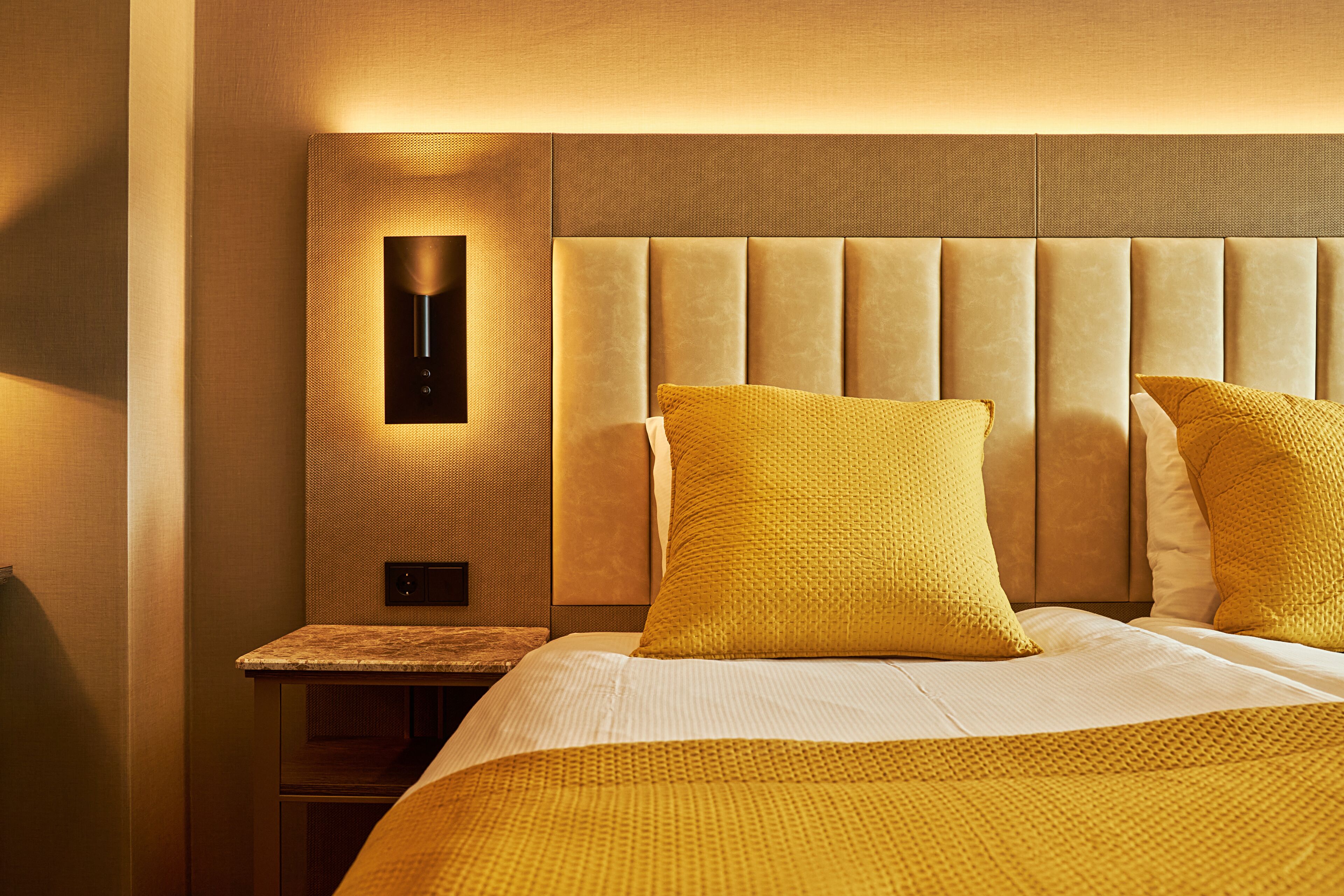 A hotel room with a large bed, a headboard with a built-in light, and a small bedside table.