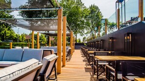 An outdoor seating area with wooden tables and chairs, a covered walkway, and a view of the surrounding greenery.