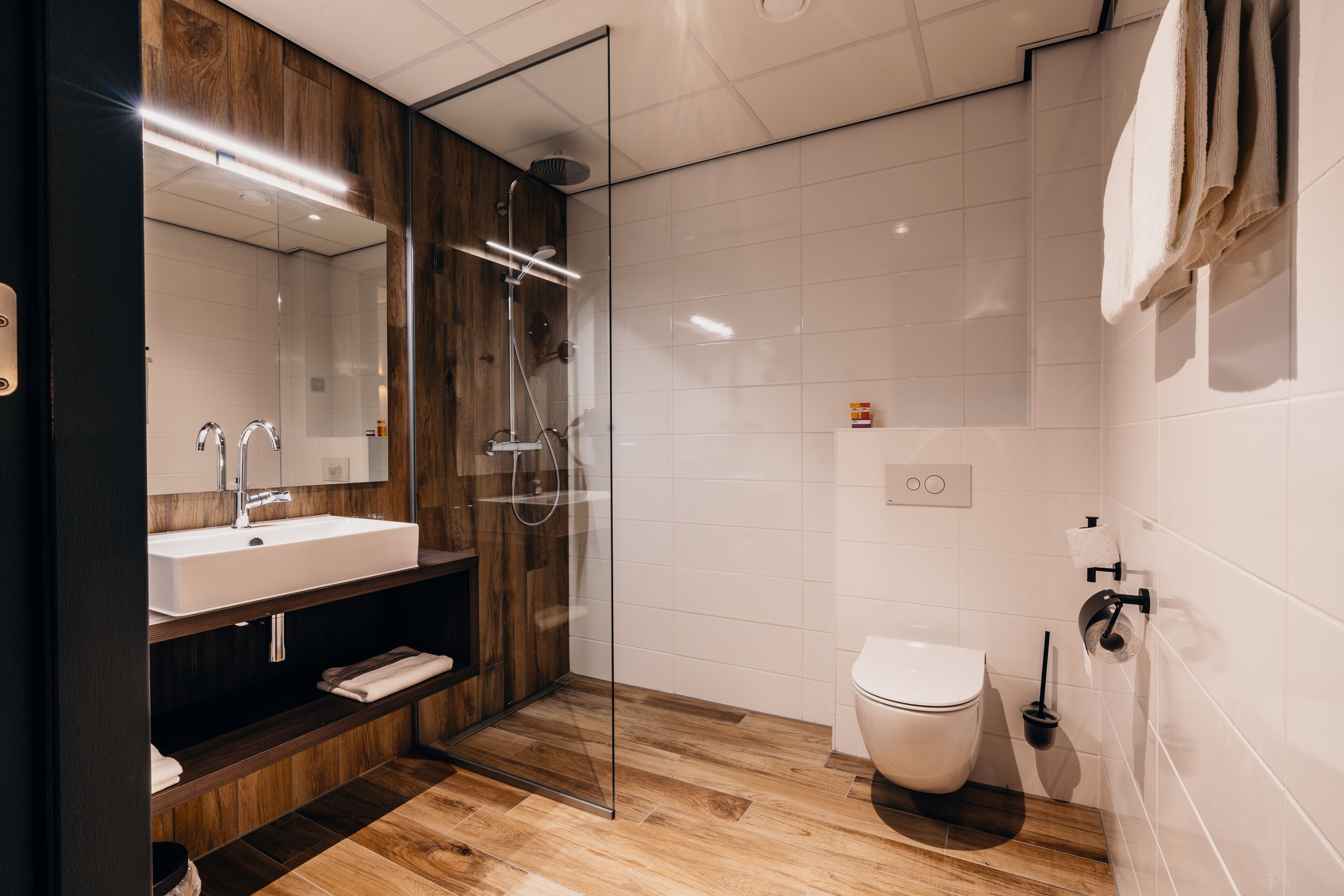 A modern bathroom with a glass-enclosed shower, a wooden vanity, a white sink, and a toilet.