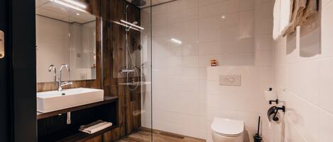 A modern bathroom with a glass-enclosed shower, a wooden vanity, a white sink, and a toilet.