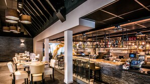 A modern bar area with a stone counter, multiple seating options, and a variety of bottles and glasses on shelves.