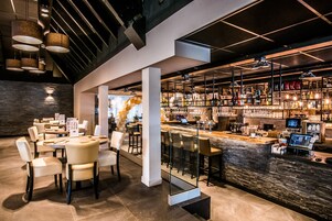 A modern bar area with a stone counter, multiple seating options, and a variety of bottles and glasses on shelves.