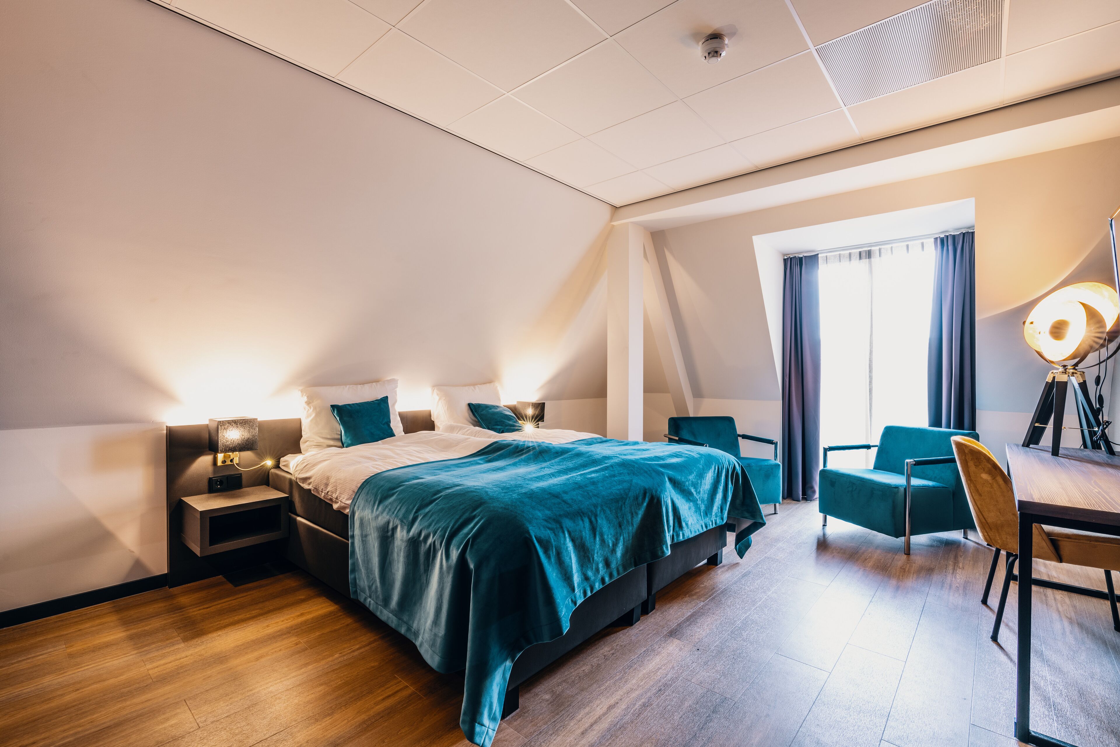 A modern hotel room with a large bed, a desk, and a chair.