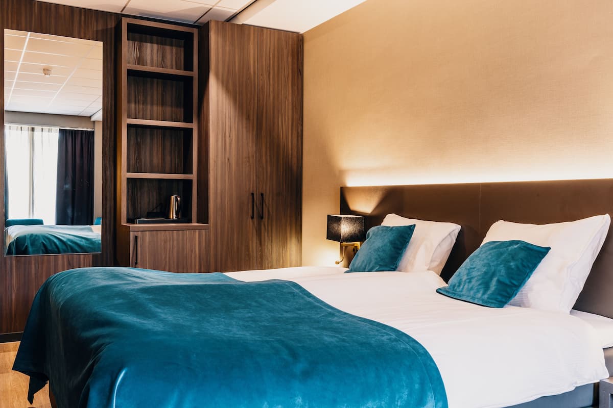 A hotel room with a large bed, a wardrobe, a nightstand, and a mirror.