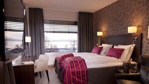 A hotel room with a large bed, two bedside tables with lamps, a desk, and a view of the outside.