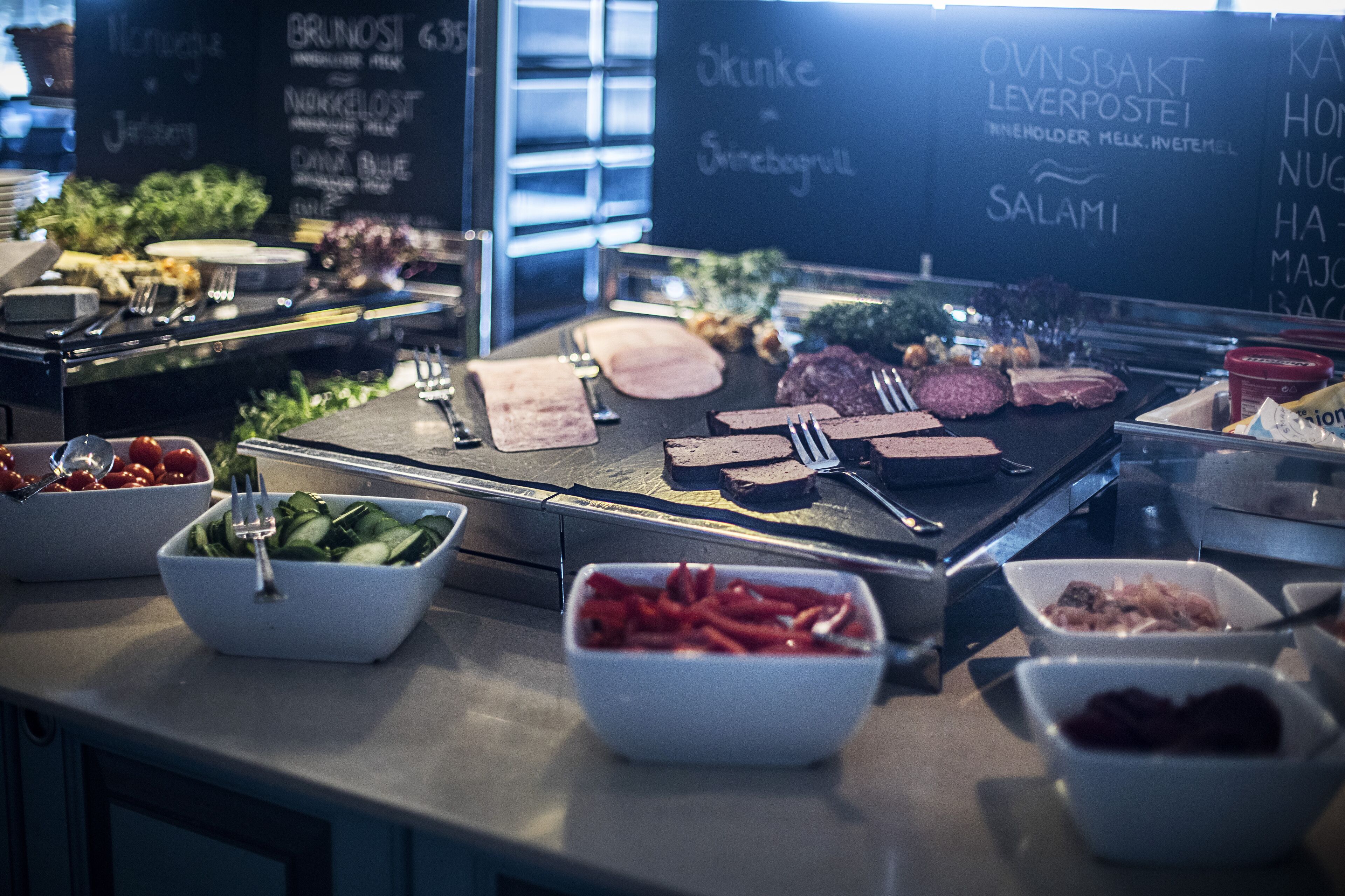 A buffet with various food items and a chalkboard menu listing dishes like 'Brunoski' and 'Ovnsbakt Leverpostei'.