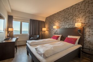 A hotel room with two beds, a desk, a chair, and a view of the outdoors.