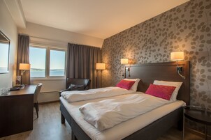 Habitación de hotel con dos camas, un escritorio, una silla y vistas al exterior.