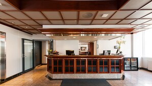 A reception area with a wooden counter, a black mat, and a tiled floor.