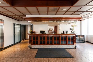 Zona de recepción con mostrador de madera, tapete negro y piso de baldosas.