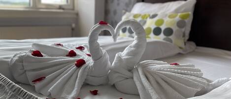 Una cama con toallas formando cisnes y pétalos de rosa esparcidos.