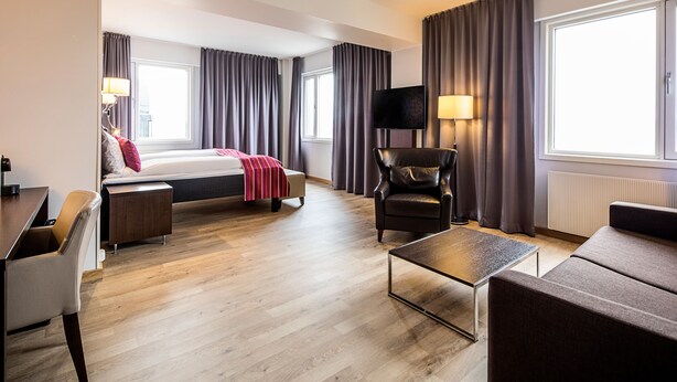 A hotel room with a bed, a desk, a chair, a sofa, a TV, and a window with curtains. - Thon Hotel Victoria Hamar (Hamar)