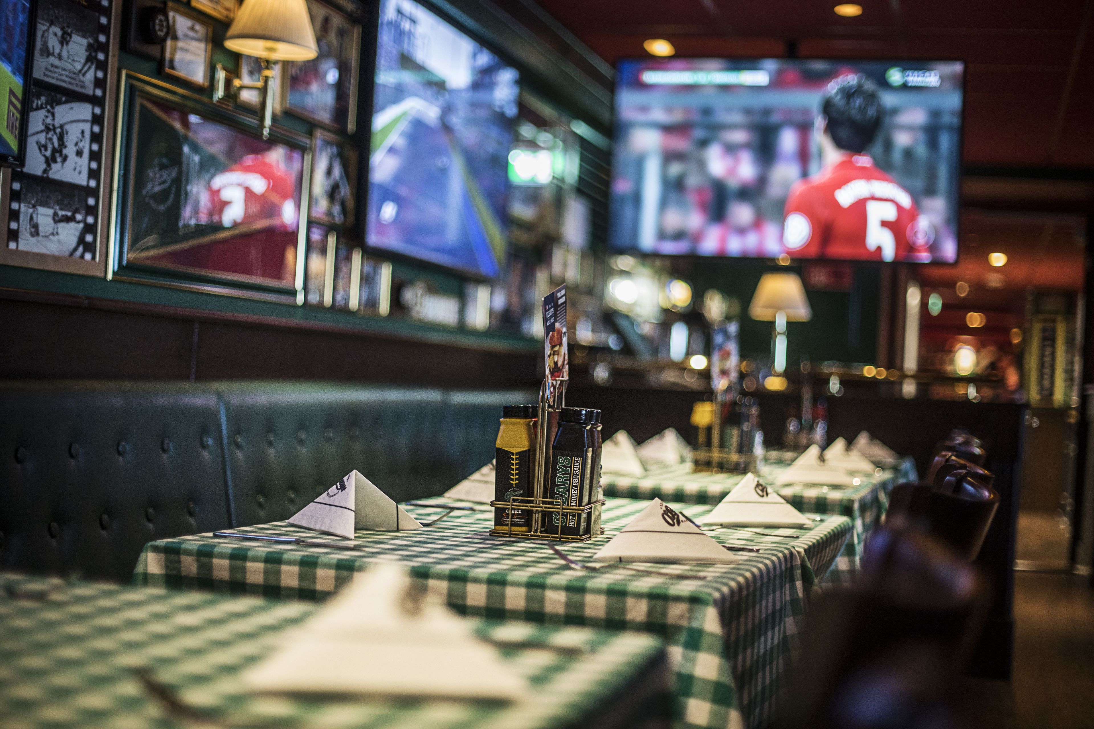A restaurant with checkered tablecloths, a bar area with a television screen displaying a sports event, and a menu stand.