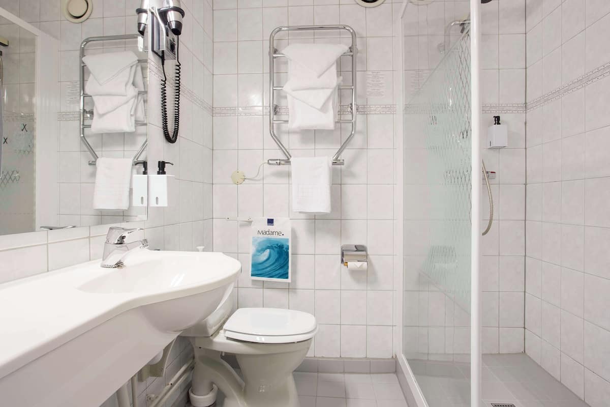 A modern bathroom with a white sink, toilet, and shower area. There are towel racks and a hand dryer.