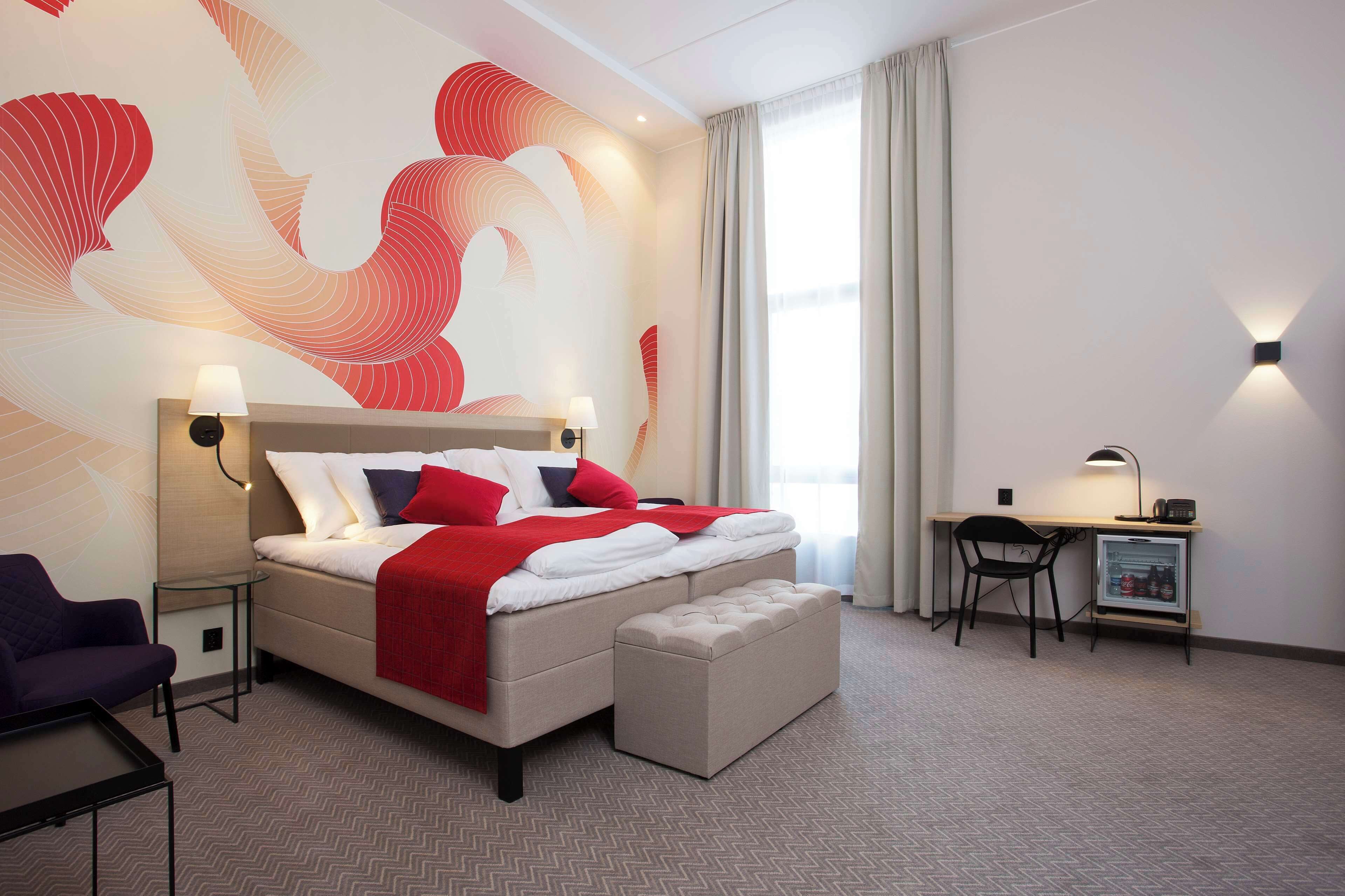 Una habitación de hotel moderna con una cama grande, un escritorio, una silla y un refrigerador pequeño.