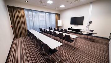 A conference room with a long table, chairs, a projector screen, and a flat-screen TV.