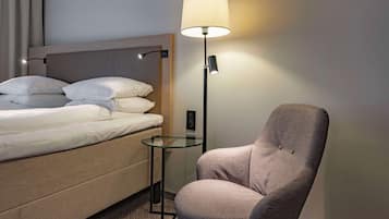 Una habitación de hotel con cama, una silla, una mesa de vidrio y una lámpara de pie.