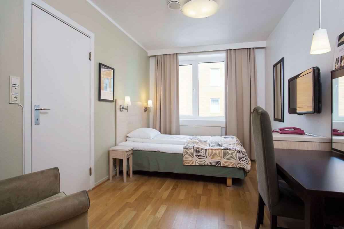 A hotel room with a bed, bedside table, chair, desk, and a window with curtains.