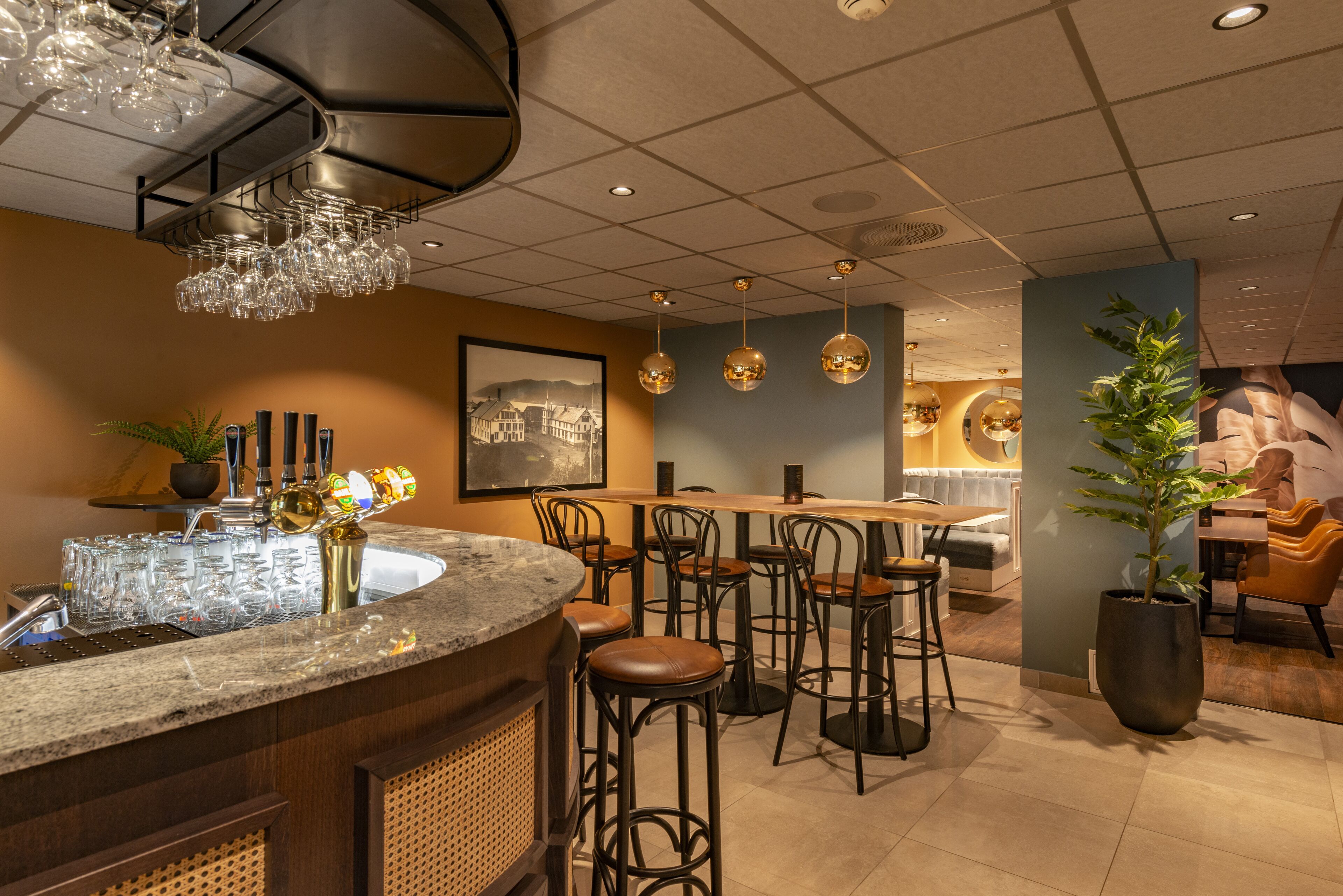 A bar area with a marble counter, stools, hanging lights, and a potted plant.