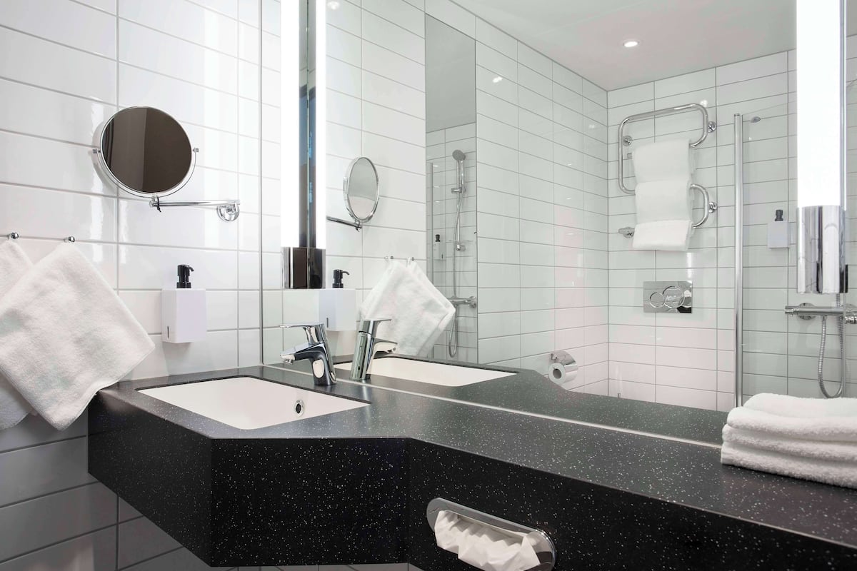 A modern bathroom with two sinks, a large mirror, and a glass-enclosed shower area.