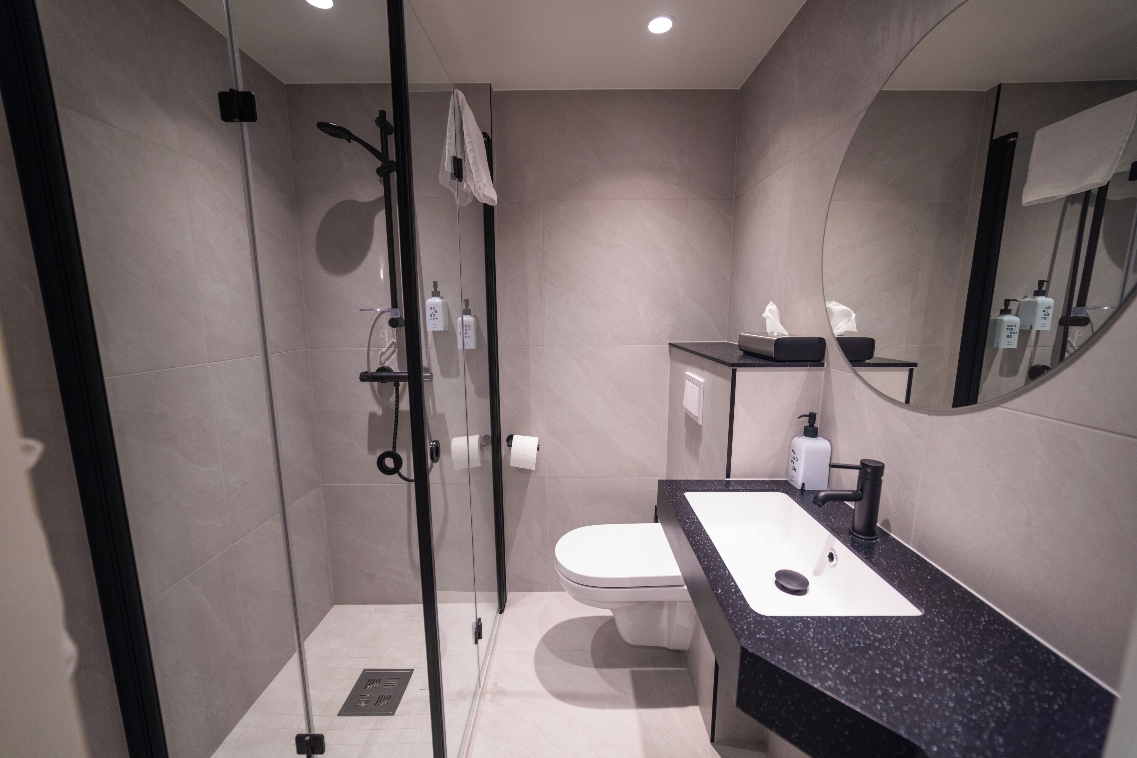 A modern bathroom with a glass-enclosed shower, a toilet, and a sink with a black countertop.